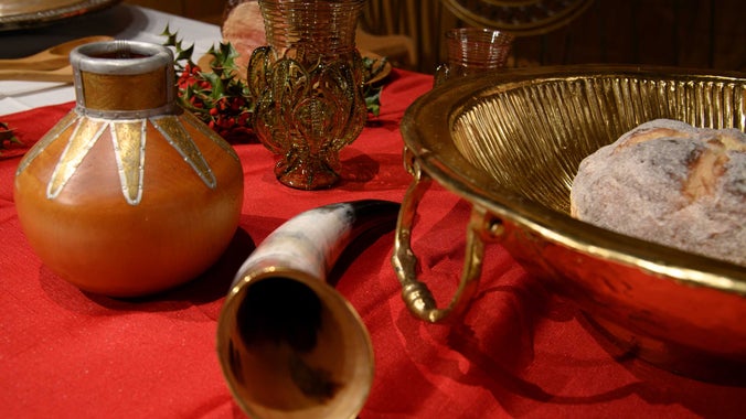 A feasting table decorated with food, holly and drinking vessels in the exhibition hall at Sutton Hoo